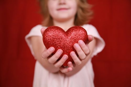 A little girl stands with a heart in her hands  symbolizing the heart of children - Charity, love, compassion